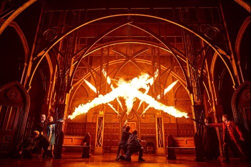 A scene from Harry Potter and the Cursed Child on Broadway in NYC, featuring a dramatic duel with fiery spells lighting up the stage, capturing the magic and intensity of the Wizarding World.